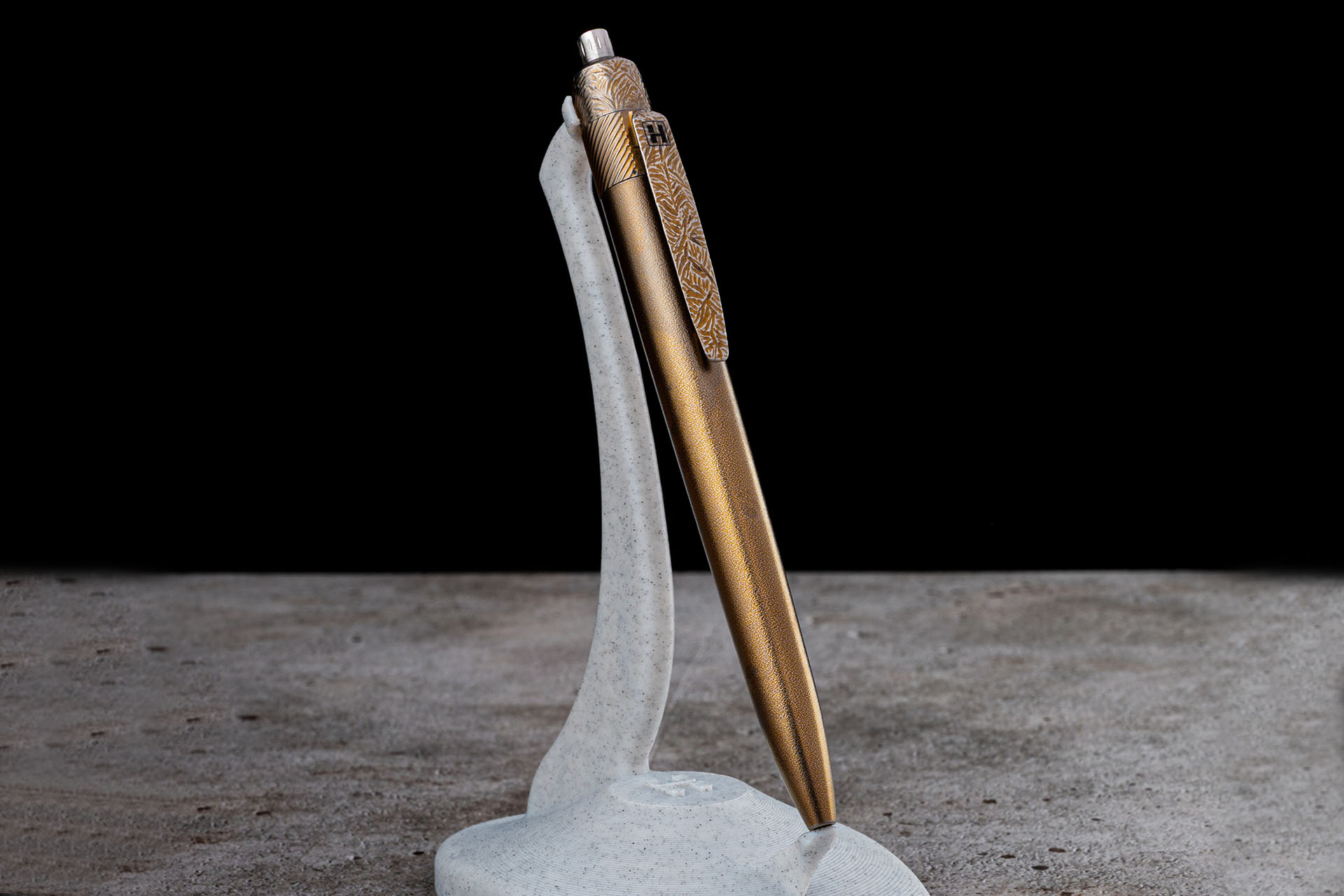 Herman Epika titanium EDC pen standing on a display stand with engraved clip and gold finish