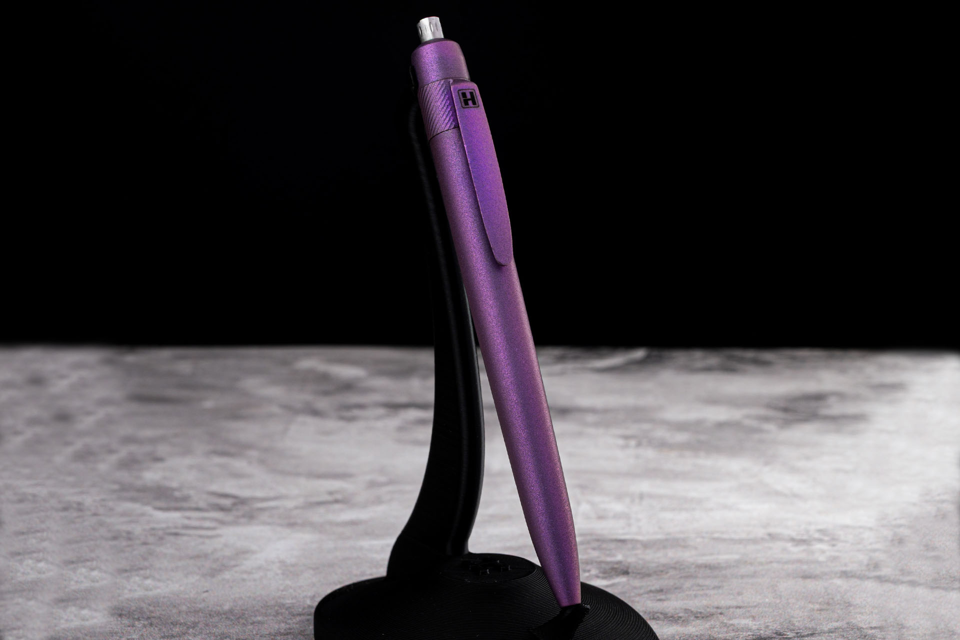 Herman Epika purple anodized titanium EDC pen displayed on a stand